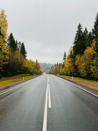 Empty road along trees and plants against sky