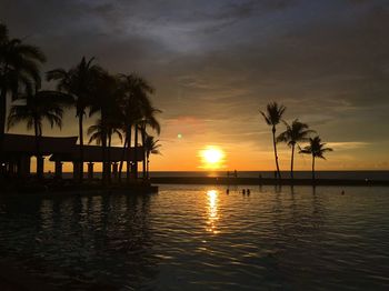 Silhouette palm trees by swimming pool against sky during sunset