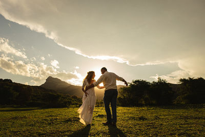 Rear view of friends standing on field against sky