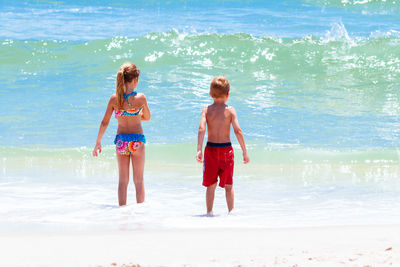 Rear view of siblings enjoying at shore during sunny day