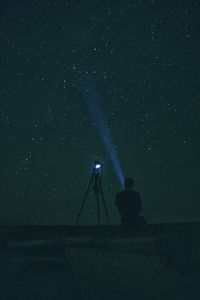 Silhouette man sitting on field against star field