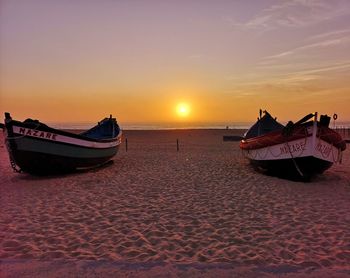 Boat moored on beach against sky during sunset
