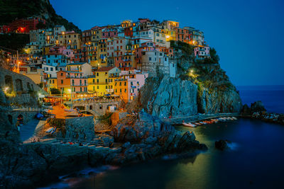 Illuminated buildings by sea against blue sky