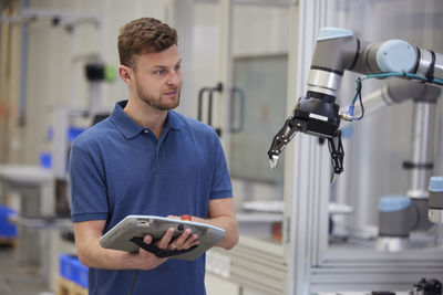 Technician operating robotic arm using equipment in industry