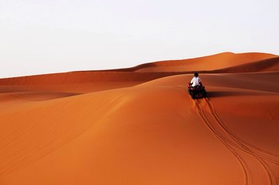 Rear view of man riding quad bike on sand dune against clear sky