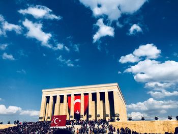 Low angle view of people on building against cloudy sky