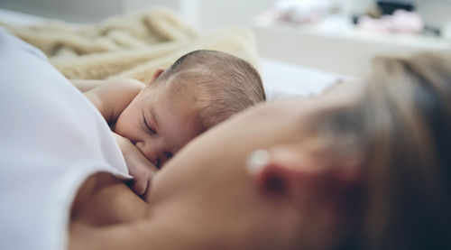 High angle view of mother breastfeeding daughter while lying on bed at home