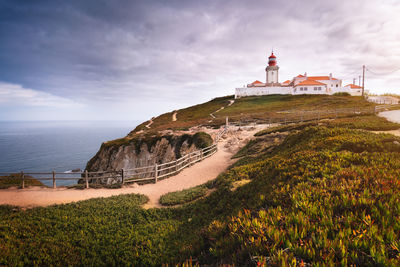 View of light house on hill by sea against sky