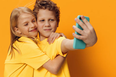 Boy taking selfie with sister against orange background