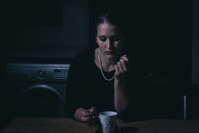 Thoughtful young woman with cup sitting at table