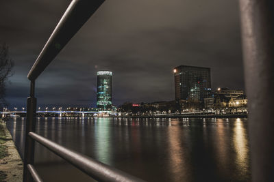 Illuminated buildings by river against sky at night