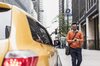 Usa, new york city, businessman approaching cab, using smart phone