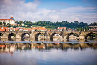 Arch bridge over river by buildings against sky