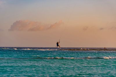 Man kiteboarding over sea against sky during sunset