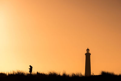 Silhouette man standing by lighthouse against sky during sunset