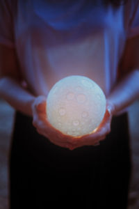 Hands of woman holding illuminated sphere shape lamp