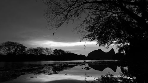 Silhouette trees by lake against sky