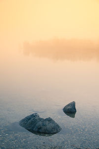 Rocks in sea against sky during sunset