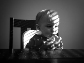 Baby girl looking away while sitting at table against wall