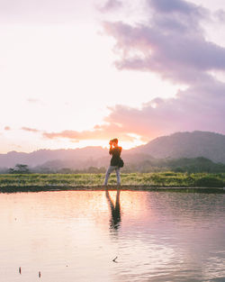 Man standing in lake against sky during sunset