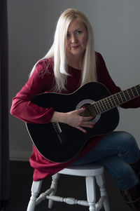 Beautiful young blonde woman in a red dress with a black guitar, favorite hobby