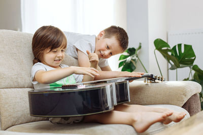 Two brothers learn to play the guitar at home. children have fun at home on the couch playing guitar