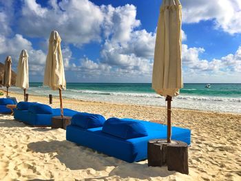 Parasols by seats at beach against blue sky