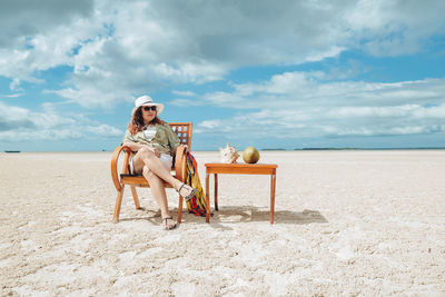 Side view of woman sitting on beach against sky
