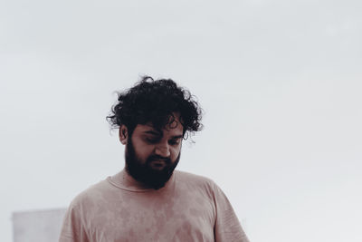 Thoughtful young bearded man standing against clear sky