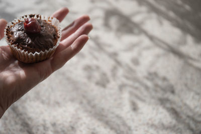 Cropped hand of woman holding cupcake on footpath