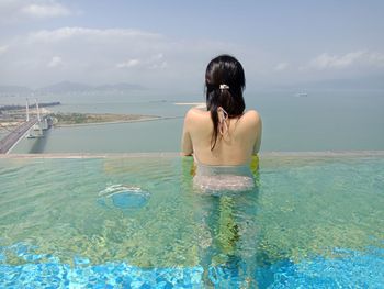 Rear view of young woman standing in infinity pool by sea