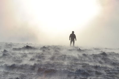 Silhouette man standing on land against sky during foggy weather