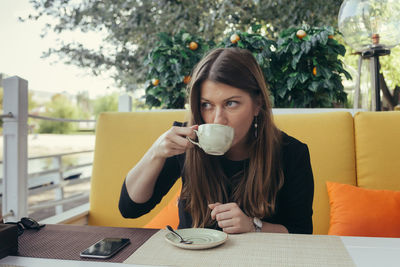 Mid adult woman drinking coffee while sitting at outdoor cafe