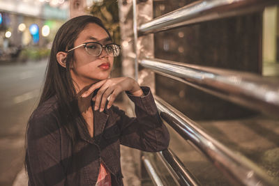 Portrait of teenage girl standing by fence on footpath