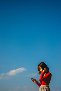 Side view of woman using smart phone against blue sky