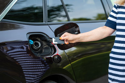 Female with credit card in front of open gas tank, fuel price rise concept, hands close-up