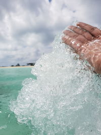 Close-up of hand by sea against sky
