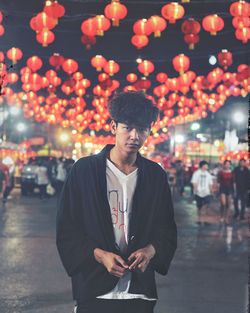 Portrait of young man standing against illuminated lanterns on road at night