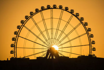 Low angle view of silhouette ferris wheel against orange sky