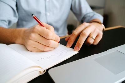 Unrecognizable crop male entrepreneur sitting at table and writing in notebook while planning business project