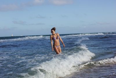 Young woman wearing bikini while standing in sea against sky