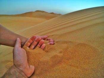 Midsection of person on sand dune in desert against sky