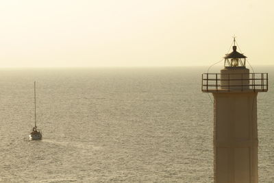 Lighthouse by sea against clear sky