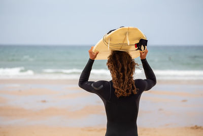 Rear view of man carrying surfboard at beach