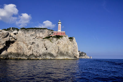 Lighthouse by sea against buildings