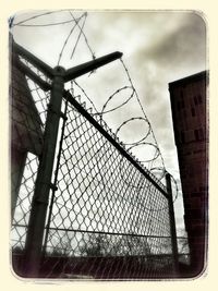Low angle view of chainlink fence against cloudy sky
