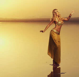 Young dancer posing on sea shore against clear sky during sunset