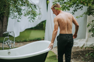 Rear view of shirtless man standing in bathroom