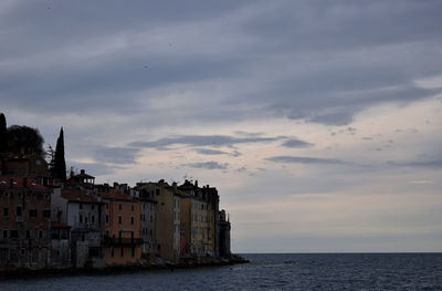 Buildings by sea against sky during sunset