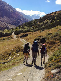 Rear view of people walking on mountain trail against sky